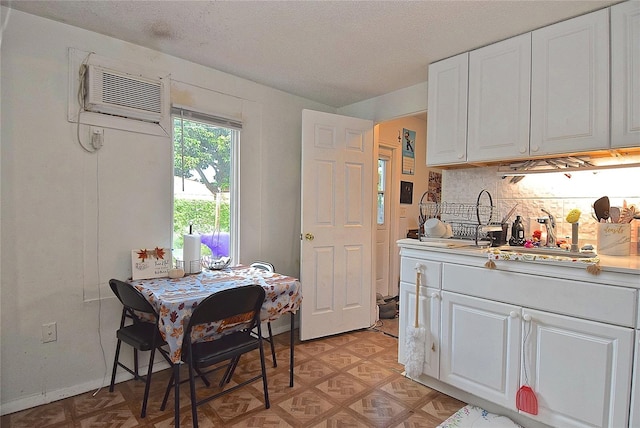 kitchen with white cabinets, a textured ceiling, tasteful backsplash, and a wall unit AC