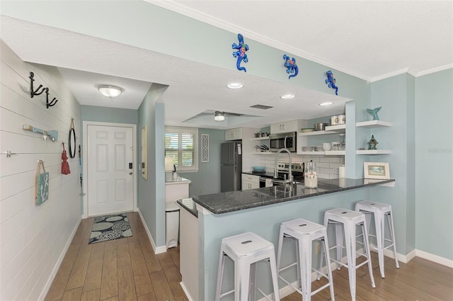 kitchen with kitchen peninsula, a textured ceiling, dark wood-type flooring, stainless steel appliances, and a kitchen bar