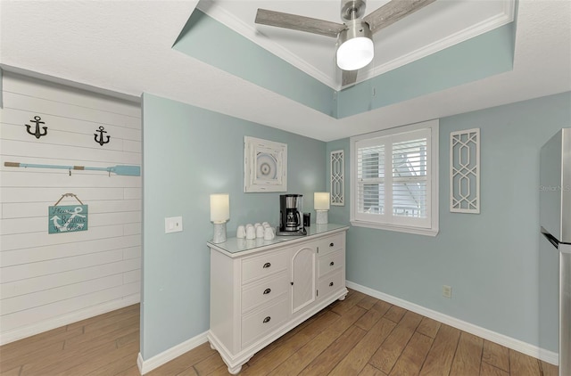 bedroom featuring light hardwood / wood-style flooring, a tray ceiling, ceiling fan, and stainless steel fridge