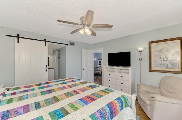 bedroom featuring ceiling fan, a textured ceiling, light hardwood / wood-style floors, and a barn door