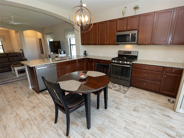 kitchen featuring tasteful backsplash, light stone countertops, sink, stainless steel appliances, and pendant lighting