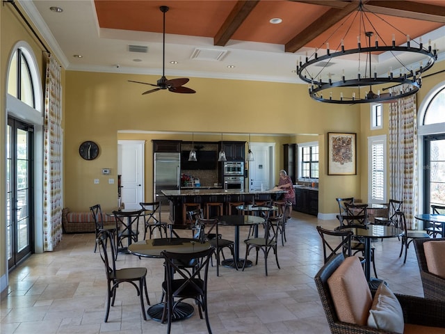 dining area featuring beamed ceiling, a high ceiling, ornamental molding, and ceiling fan with notable chandelier