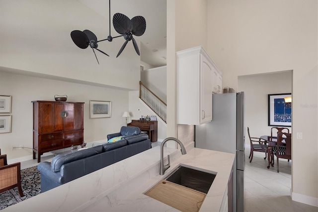 kitchen featuring ceiling fan, white cabinets, stainless steel fridge, sink, and a towering ceiling