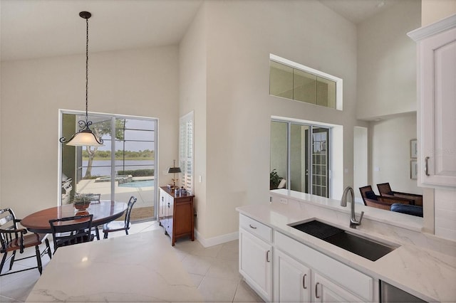 kitchen featuring a towering ceiling, hanging light fixtures, white cabinets, and sink