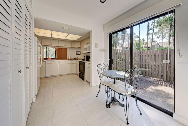 kitchen featuring a healthy amount of sunlight, white appliances, light tile patterned flooring, and white cabinets