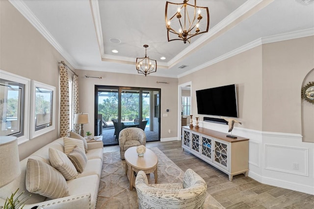 living room with a notable chandelier, light hardwood / wood-style floors, a raised ceiling, and ornamental molding