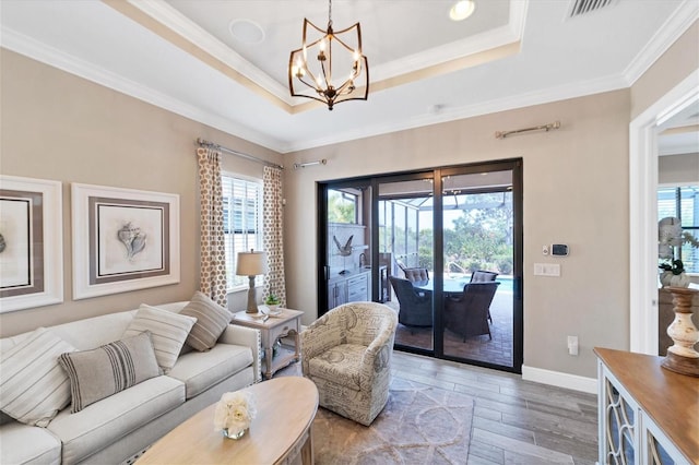 living room featuring hardwood / wood-style flooring, a raised ceiling, ornamental molding, and a notable chandelier