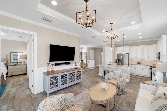 living room featuring a raised ceiling, light hardwood / wood-style flooring, ornamental molding, and sink