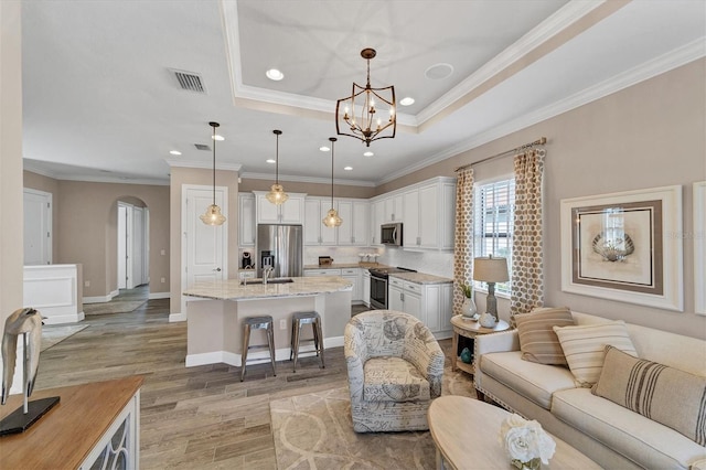 living room featuring a notable chandelier, light hardwood / wood-style floors, a raised ceiling, and ornamental molding