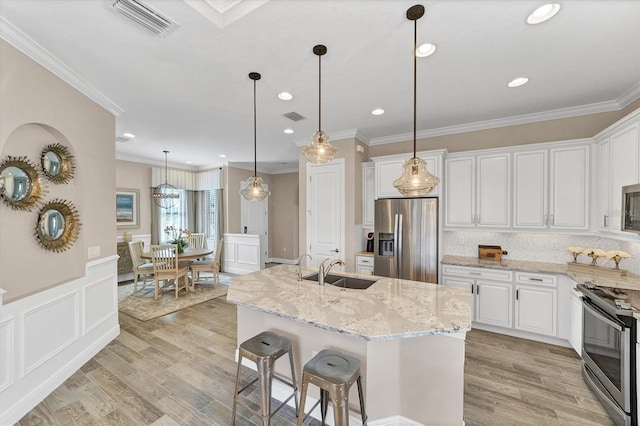 kitchen with white cabinets, stainless steel appliances, light hardwood / wood-style flooring, and a center island with sink