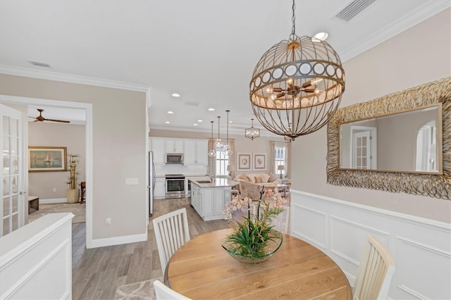 dining room featuring sink, light hardwood / wood-style flooring, ceiling fan with notable chandelier, and ornamental molding