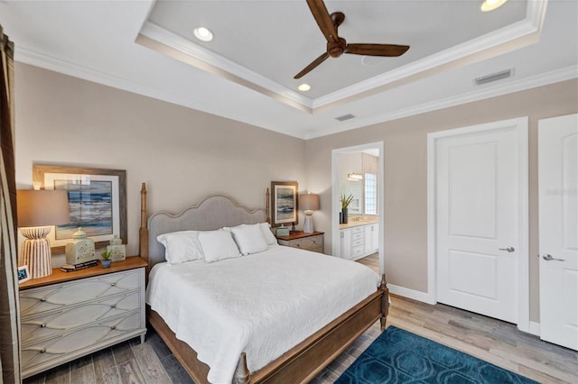 bedroom with ceiling fan, a raised ceiling, wood-type flooring, and ensuite bath