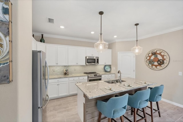 kitchen with an island with sink, stainless steel appliances, pendant lighting, white cabinets, and light stone counters