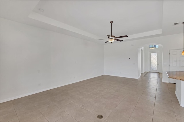 empty room with light tile patterned floors, a tray ceiling, and ceiling fan