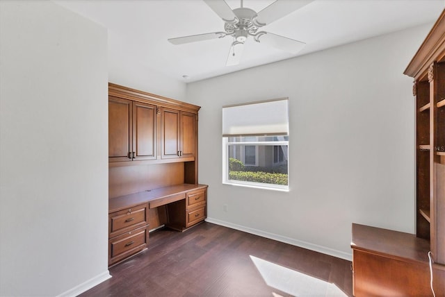 unfurnished office featuring ceiling fan, built in desk, and dark wood-type flooring