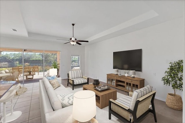 living room featuring ceiling fan, light tile patterned flooring, and a tray ceiling