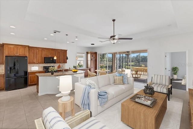 living room featuring ceiling fan, light tile patterned flooring, a raised ceiling, and sink