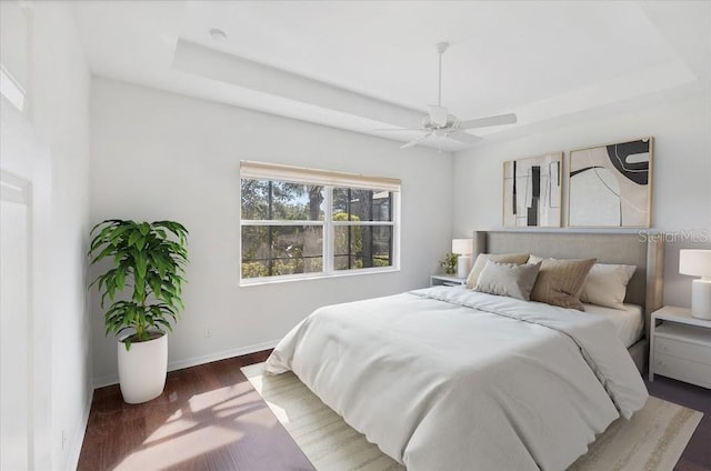 bedroom featuring ceiling fan, dark wood-type flooring, and a tray ceiling