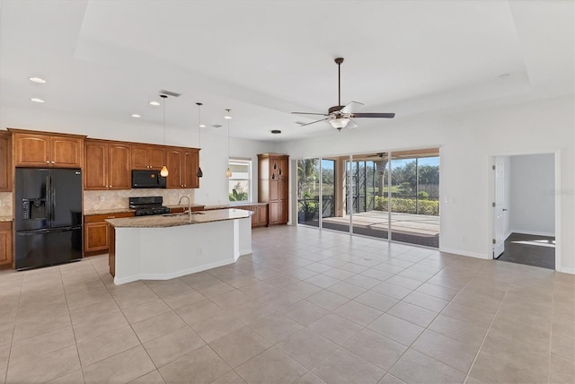 kitchen with light stone counters, a kitchen island with sink, sink, black appliances, and light tile patterned floors