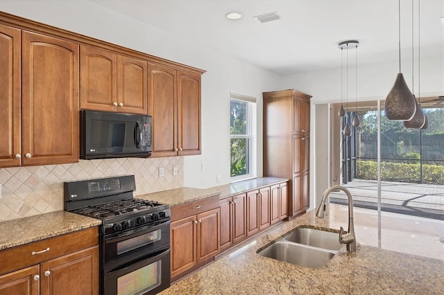 kitchen with decorative backsplash, light stone counters, sink, black appliances, and hanging light fixtures