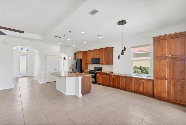 kitchen with light stone countertops, sink, black appliances, pendant lighting, and a kitchen island