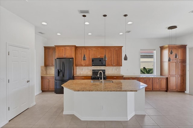 kitchen featuring light stone countertops, a kitchen island with sink, hanging light fixtures, and black appliances