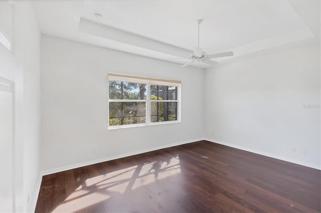 unfurnished room with ceiling fan, a raised ceiling, and dark wood-type flooring