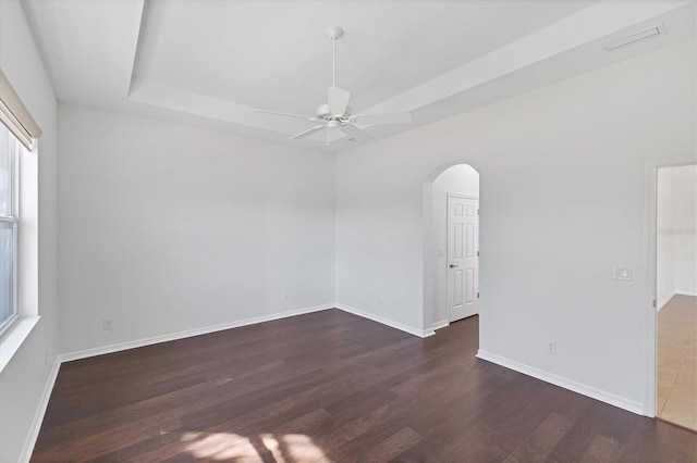 unfurnished room featuring a healthy amount of sunlight, dark hardwood / wood-style floors, ceiling fan, and a tray ceiling