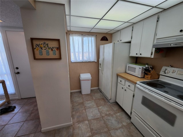 kitchen with white appliances, light tile patterned flooring, a drop ceiling, white cabinetry, and exhaust hood