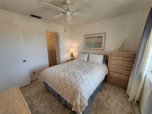 carpeted bedroom featuring a spacious closet, a textured ceiling, a closet, and ceiling fan