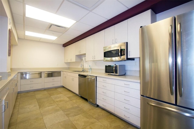 kitchen with appliances with stainless steel finishes, a drop ceiling, white cabinetry, and sink