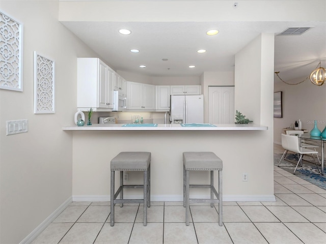 kitchen featuring white cabinets, a kitchen bar, white appliances, and kitchen peninsula