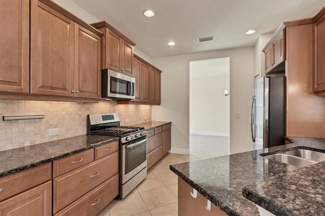 kitchen with dark stone counters, appliances with stainless steel finishes, light tile patterned floors, and tasteful backsplash