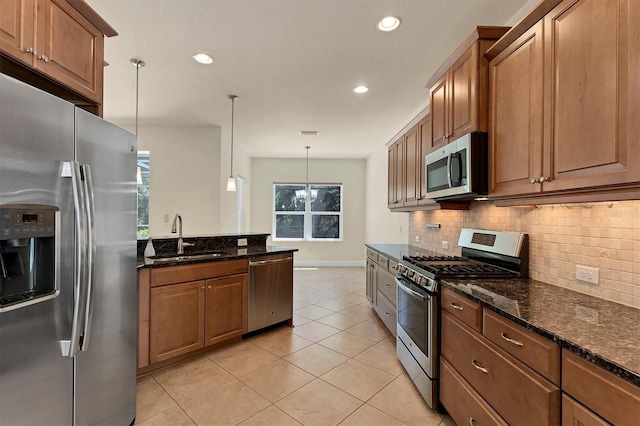 kitchen with decorative backsplash, stainless steel appliances, dark stone countertops, sink, and pendant lighting