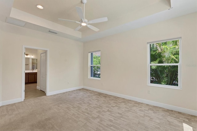 empty room with ceiling fan, a tray ceiling, and light carpet