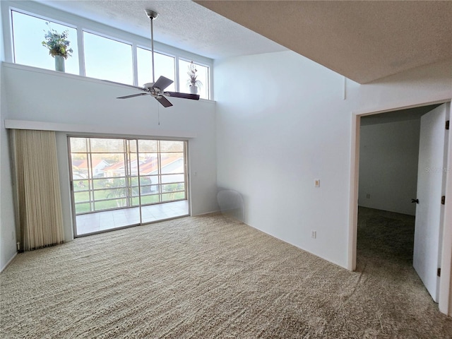 unfurnished living room with ceiling fan, carpet flooring, a high ceiling, and a textured ceiling