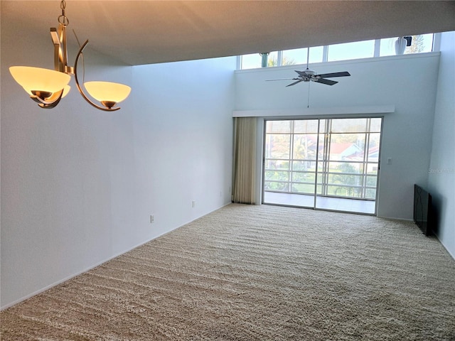 unfurnished room featuring carpet floors, a towering ceiling, and ceiling fan with notable chandelier