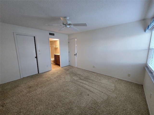 unfurnished bedroom featuring ceiling fan, a textured ceiling, connected bathroom, and light colored carpet