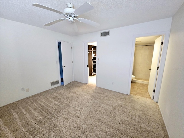 unfurnished bedroom featuring ensuite bath, light carpet, a textured ceiling, and a spacious closet