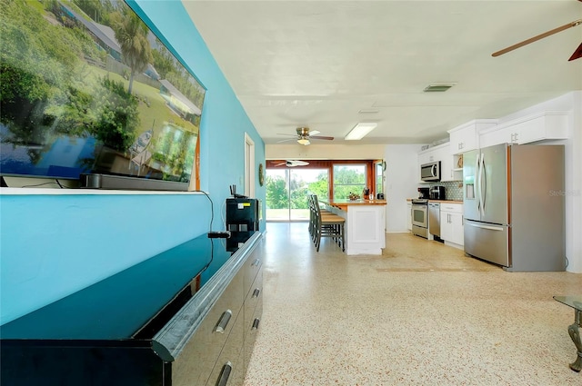 interior space with ceiling fan, stainless steel appliances, a kitchen bar, and white cabinets