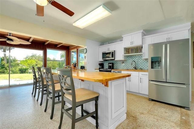 kitchen with white cabinets, backsplash, appliances with stainless steel finishes, a breakfast bar area, and wooden counters