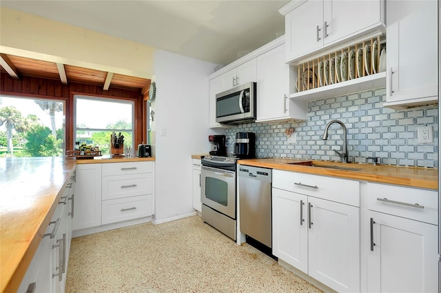 kitchen with beam ceiling, appliances with stainless steel finishes, white cabinetry, butcher block counters, and sink