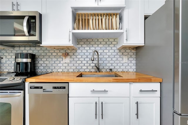 kitchen featuring stainless steel appliances, sink, white cabinetry, butcher block countertops, and tasteful backsplash