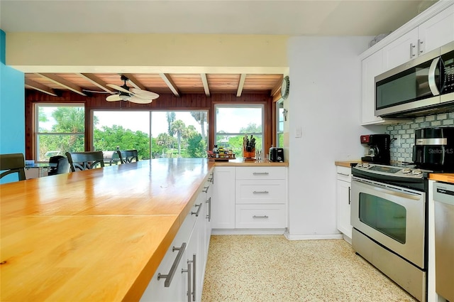 kitchen featuring beam ceiling, appliances with stainless steel finishes, white cabinetry, butcher block countertops, and ceiling fan