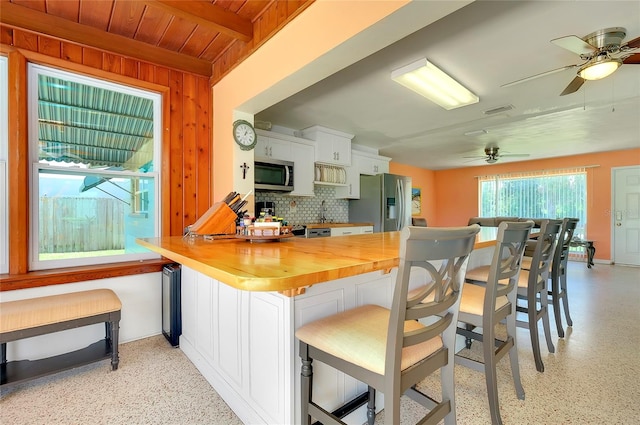 kitchen featuring decorative backsplash, appliances with stainless steel finishes, wood counters, white cabinetry, and beamed ceiling