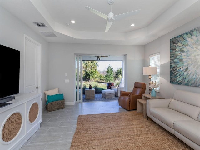 living room with ceiling fan and a raised ceiling