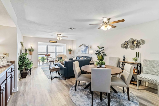 dining area featuring a textured ceiling, light wood-type flooring, and ceiling fan