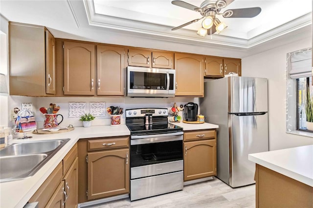 kitchen with stainless steel appliances, a tray ceiling, light wood-type flooring, and ceiling fan