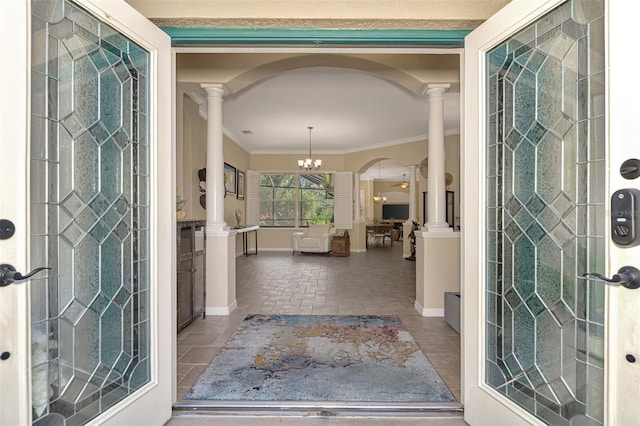 tiled entryway with ornate columns, crown molding, and an inviting chandelier