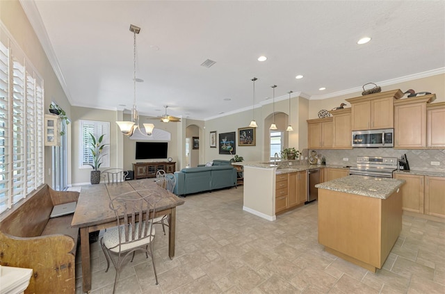 kitchen with light brown cabinets, hanging light fixtures, appliances with stainless steel finishes, light stone counters, and kitchen peninsula